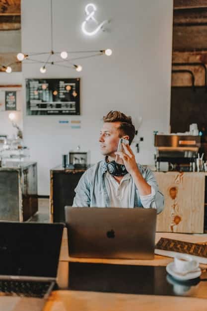 Homme concentré, téléphone à l’oreille et ordinateur ouvert devant lui, effectuant des démarches pour devenir freelance.