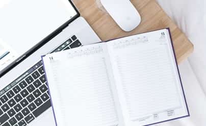 Ordinateur et bloc-notes symbolisant les moyens de coordination, la planification et le suivi des activités récréatives en entreprise.