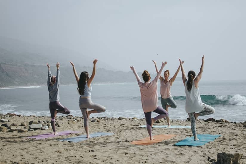 Salariées pratiquant de la gymnastique sur la plage, illustration d’un projet collectif de sortie détente organisé par la commission loisirs.
